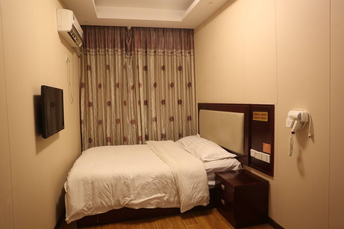 Habitación de hotel con cama, televisión montada en la pared, aire acondicionado, teléfono y una mesita.