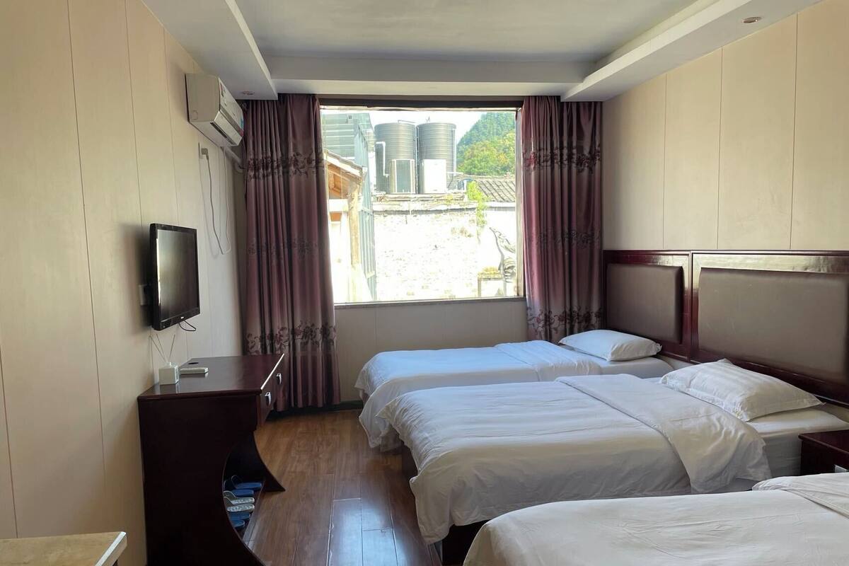 Habitación de hotel con dos camas, televisor, piso de madera y ventana con cortinas.