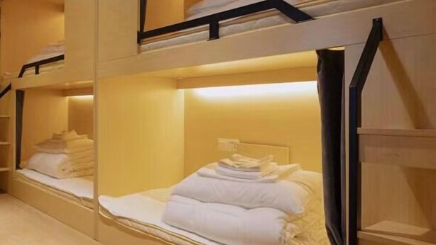 A hotel room with bunk beds, each with a headboard and a shelf above. - Biancheng International Youth Hostel (Xiangxi)