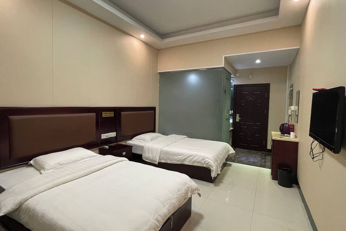 Habitación de hotel con dos camas, un televisor, un escritorio y una puerta que da a otra habitación.