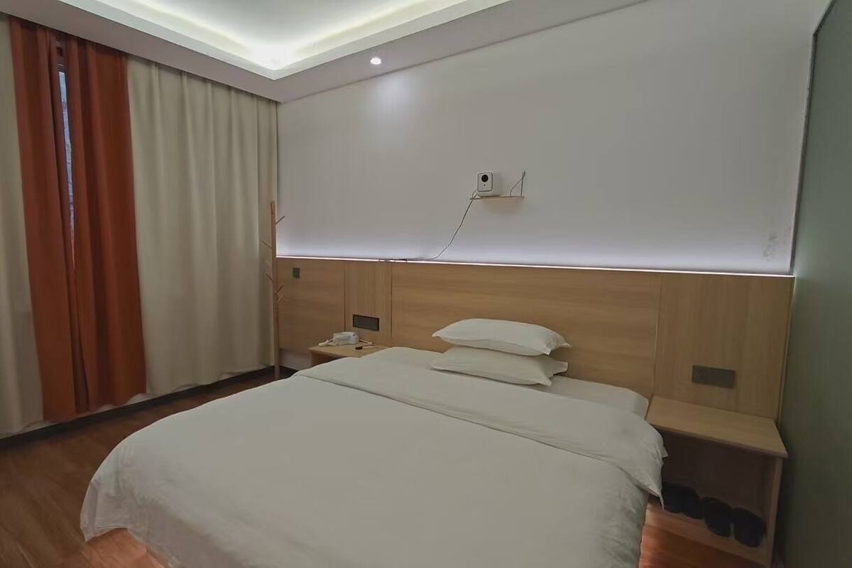 Habitación de hotel con una cama grande, una mesita de noche con un teléfono y una lámpara fijada a la pared.