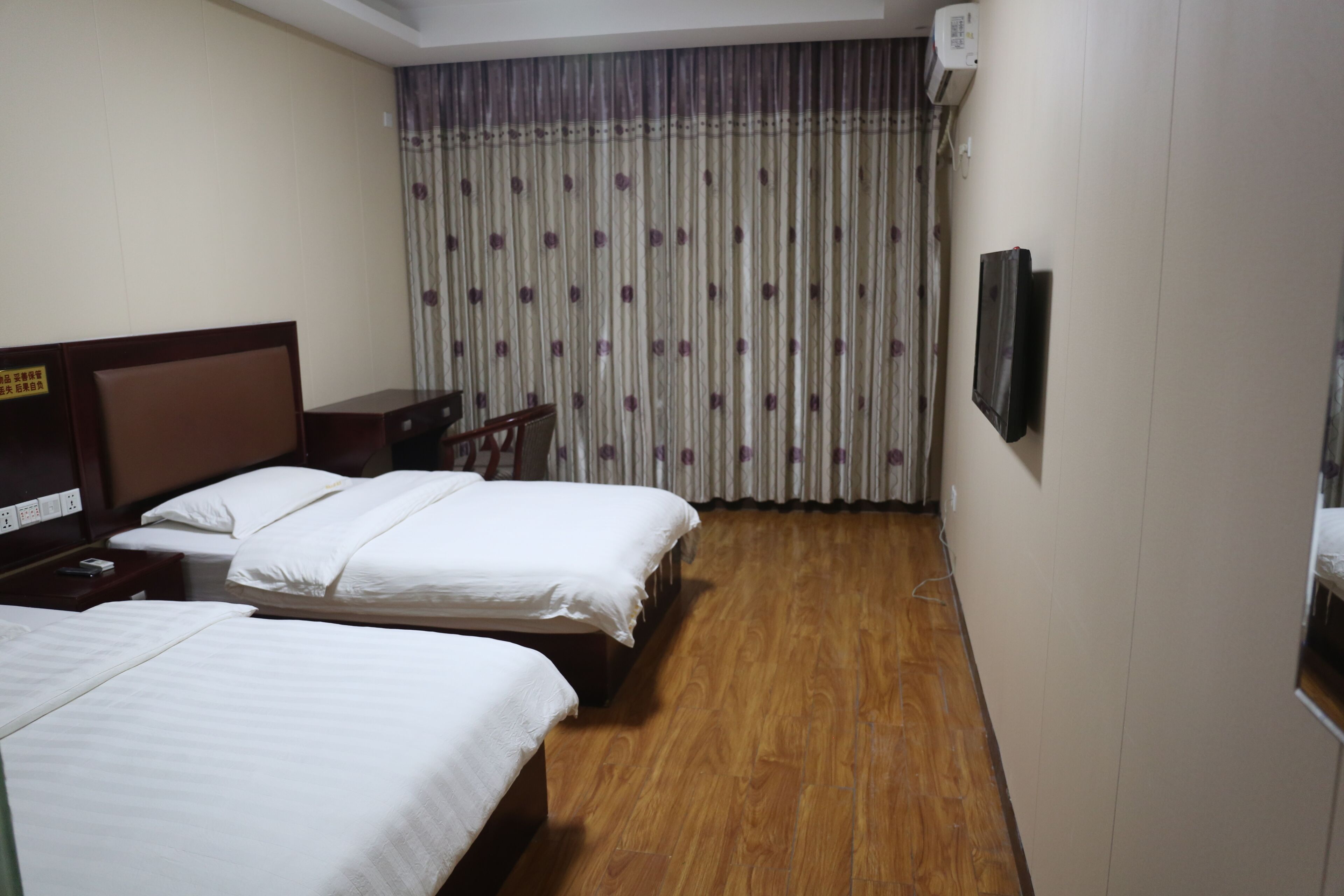 A hotel room with two beds, a desk, a chair, a TV, and a curtain with a floral pattern.
