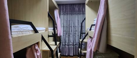 A dormitory room with bunk beds, wooden flooring, and a ceiling light.