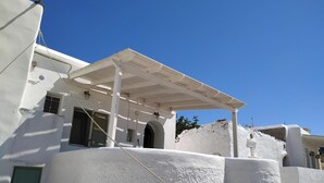 Un bâtiment blanc doté d’un patio couvert, d’une porte verte et surplombé d’un ciel bleu clair.