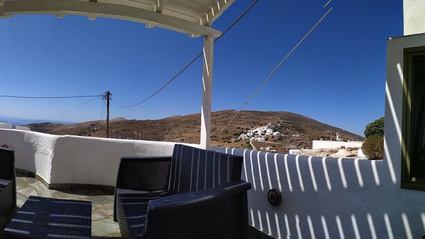 Un espace extérieur aménagé avec des chaises et une pergola, offrant une vue sur une colline et la mer.