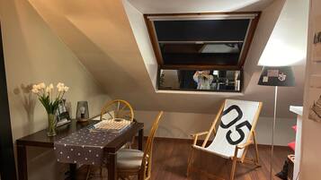 Ein kleiner Raum mit schrägverdeckter Decke, einem Esstisch mit Stühlen, einem Fenster und einer Lampe.