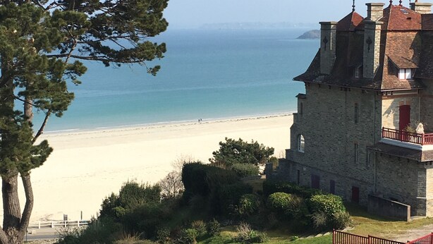 A coastal building with a stone facade, a balcony with a red railing, and a view of the beach and sea. - Apartment 'Newport Vue Mer' with Sea View, Private Terrace and Wi-Fi (Saint-Cast-le-Guildo)
