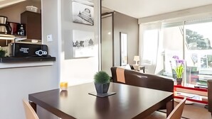 A dining area with a wooden table, beige chairs, a small potted plant, and a kitchen in the background. - Apartment 'Newport Vue Mer' with Sea View, Private Terrace and Wi-Fi (Saint-Cast-le-Guildo)