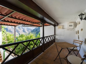 Un balcón con vistas a montañas, una mesa con sillas y una lámpara fijada a la pared.