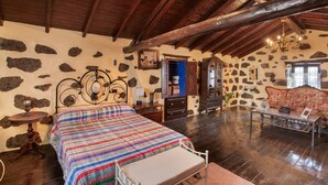 A rustic room with a bed, a sofa, a chandelier, and stone walls.