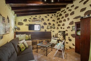 Una habitación acogedora con pared de piedra, techo de madera, un sofá, una mesa y una silla.