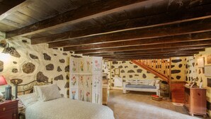 Une chambre à coucher avec un lit, des poutres en bois, des murs en pierre, un escalier et une commode.