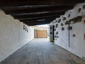 A corridor with a stone wall on one side and a wooden ceiling on the other, leading to a wooden gate.