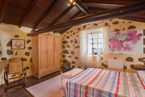 A room with a bed, wooden wardrobe, stone wall, and a window with curtains.