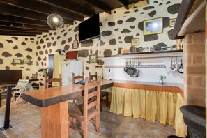 Una cocina rústica con paredes de piedra, una mesa de madera, sillas, un televisor y una estufa.