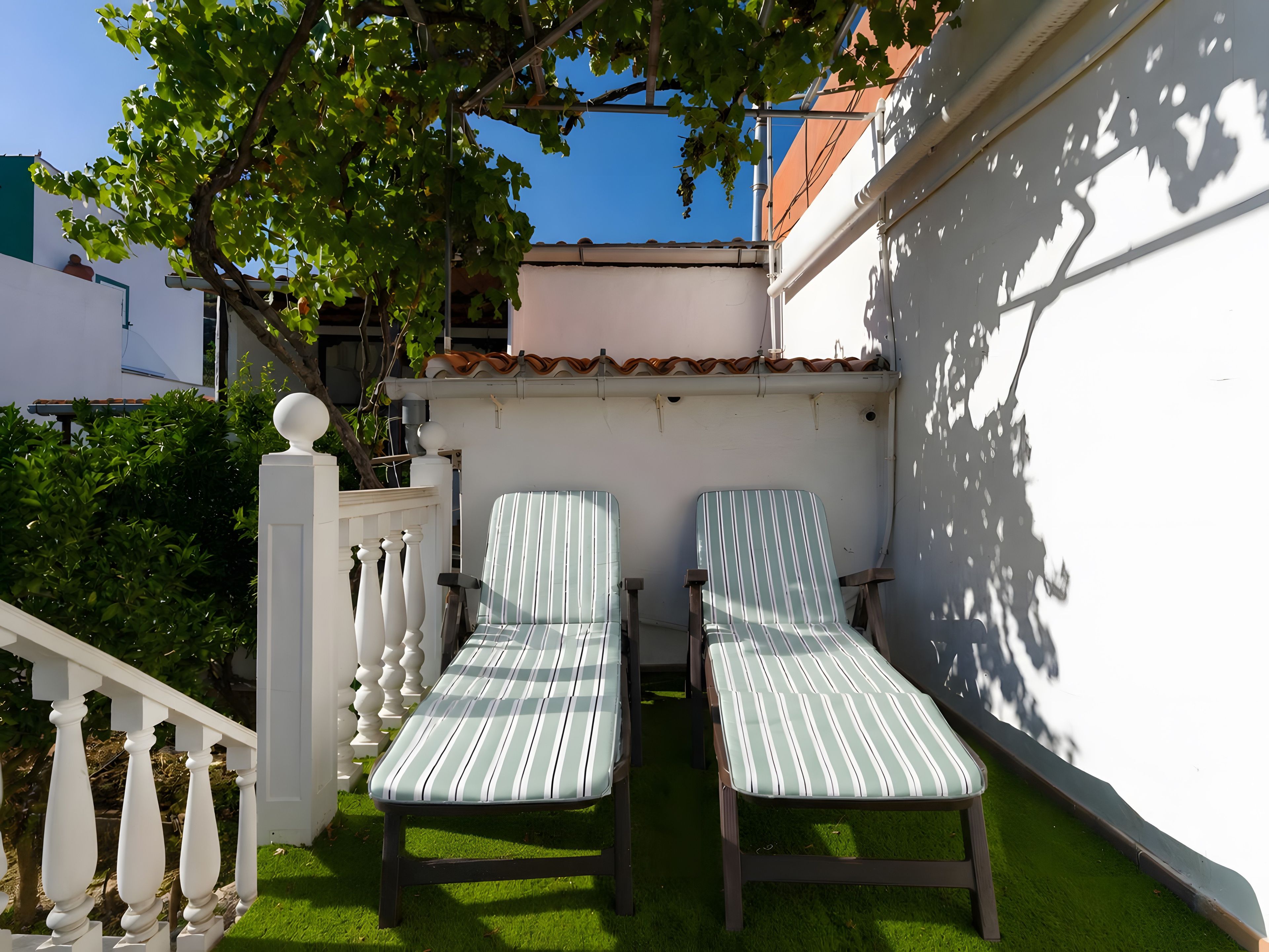 Two striped lounge chairs on a green lawn, a white balustrade, and a white wall with a tiled roof.