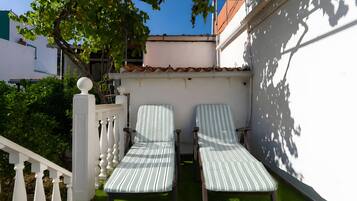 Two striped lounge chairs on a green lawn, a white balustrade, and a white wall with a tiled roof.