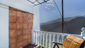 A balcony with a white railing, a wooden bench, and a view of distant mountains.