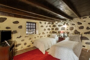 Un dormitorio con paredes de piedra, vigas de madera, dos camas, un televisor y una alfombra roja.