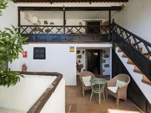 A two-story building with a balcony, a staircase, wicker furniture, and a fire extinguisher.