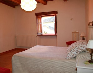 A bedroom with a bed, a window, a radiator, a lamp, and a wooden ceiling.