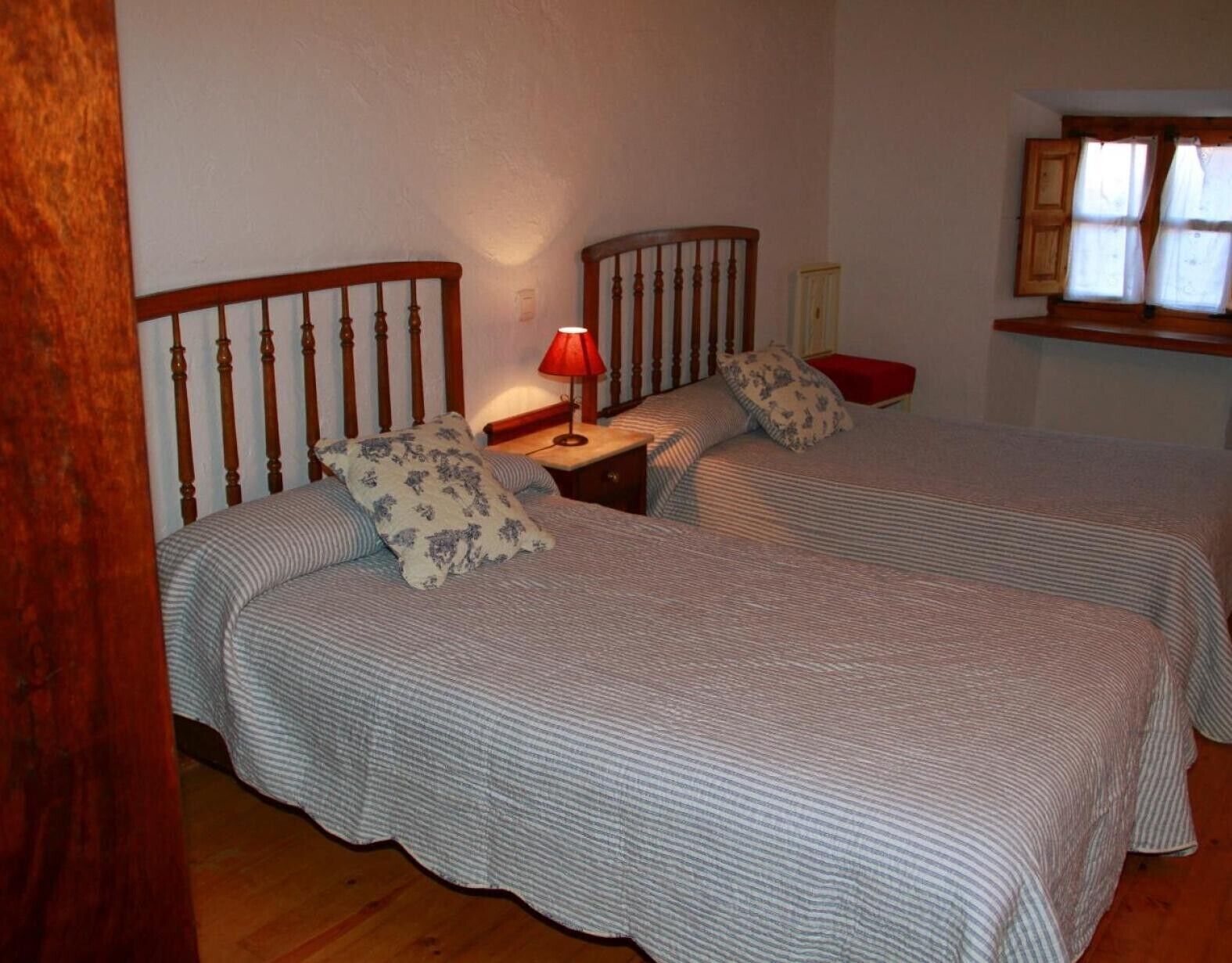 A bedroom with two beds, a nightstand with a lamp, and a window with curtains.