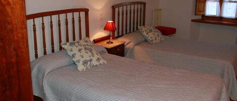 A bedroom with two beds, a nightstand with a lamp, and a window with curtains.