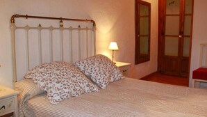 A bedroom with a bed, a nightstand, a lamp, a wooden door, and a window.