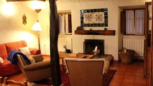 A cozy living room with a fireplace, wooden beams, a sofa, and a lamp.