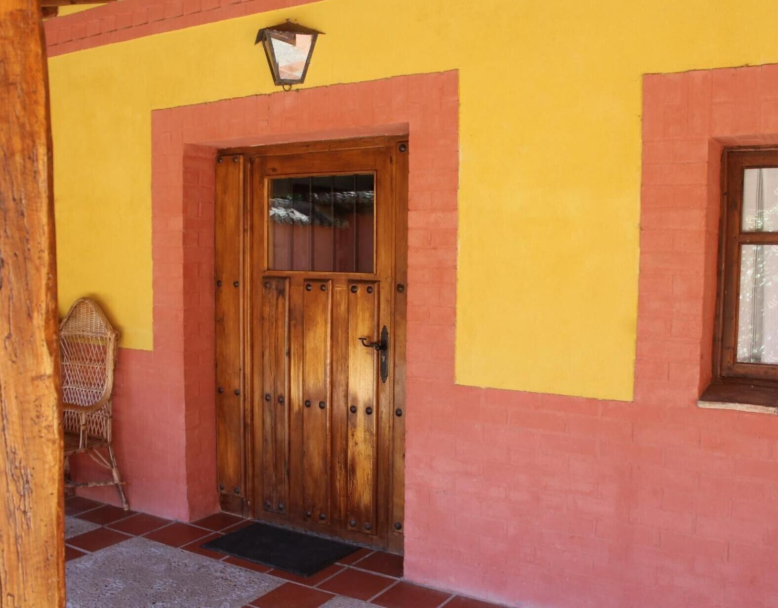 Una porta di legno con maniglia in metallo, una sedia in vimini e una piccola finestra con tenda.