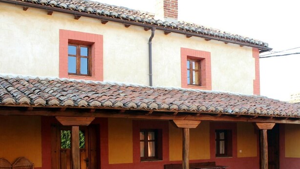 A building with a tiled roof, a covered patio with a table and chairs, and a wooden door.