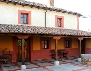 Un edificio con techo de tejas, un porche cubierto con una mesa y sillas, y una puerta de madera.