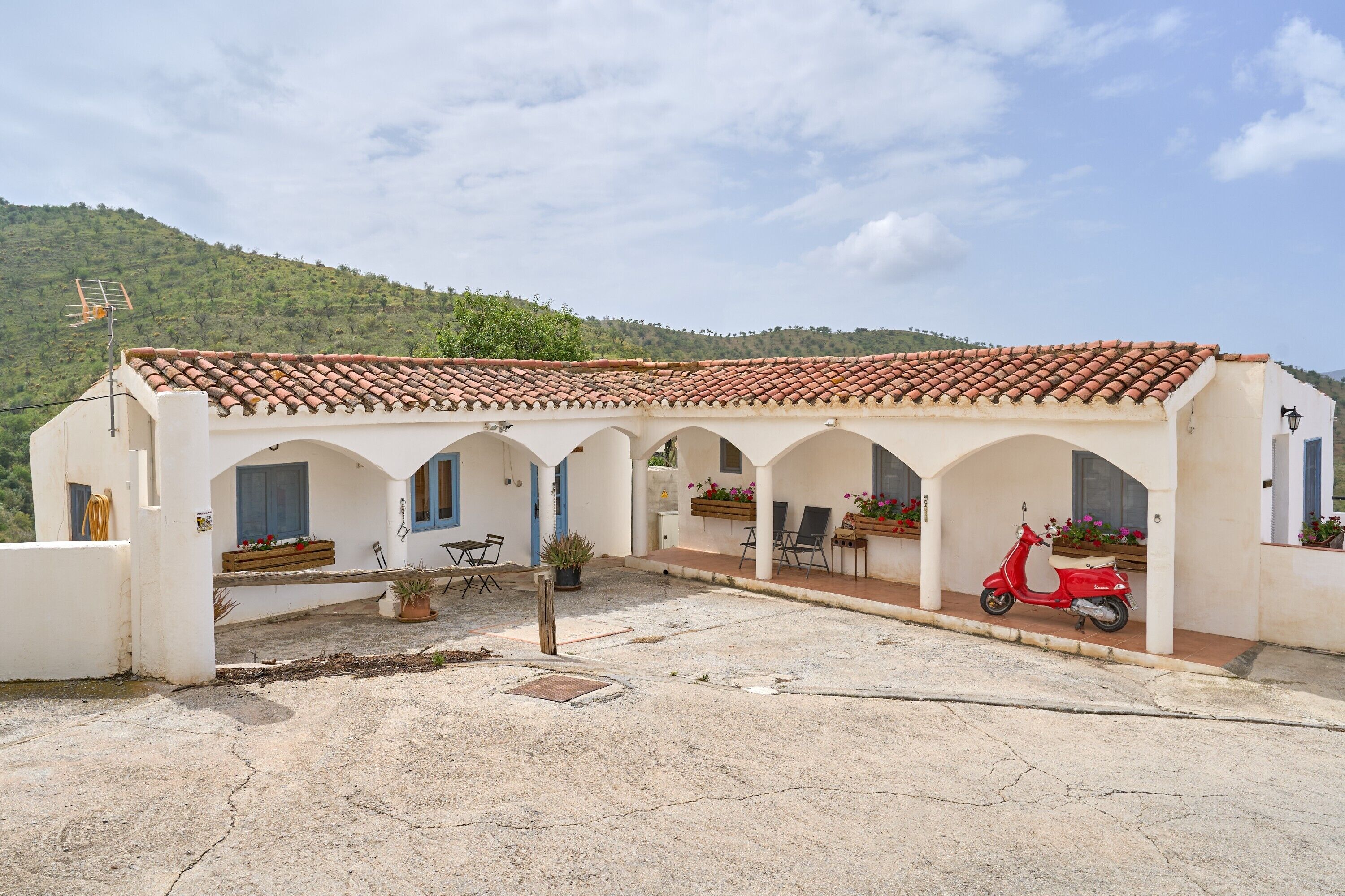 A building with a tiled roof, multiple arches, and a red scooter parked outside.