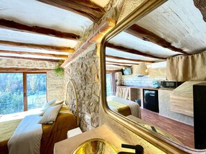 A rustic interior with a stone wall, a bed with white bedding, a wooden ceiling, and a kitchen area with a microwave and a television. - Apartment 'Duende' with Mountain View, Balcony and Air Conditioning (Olba)
