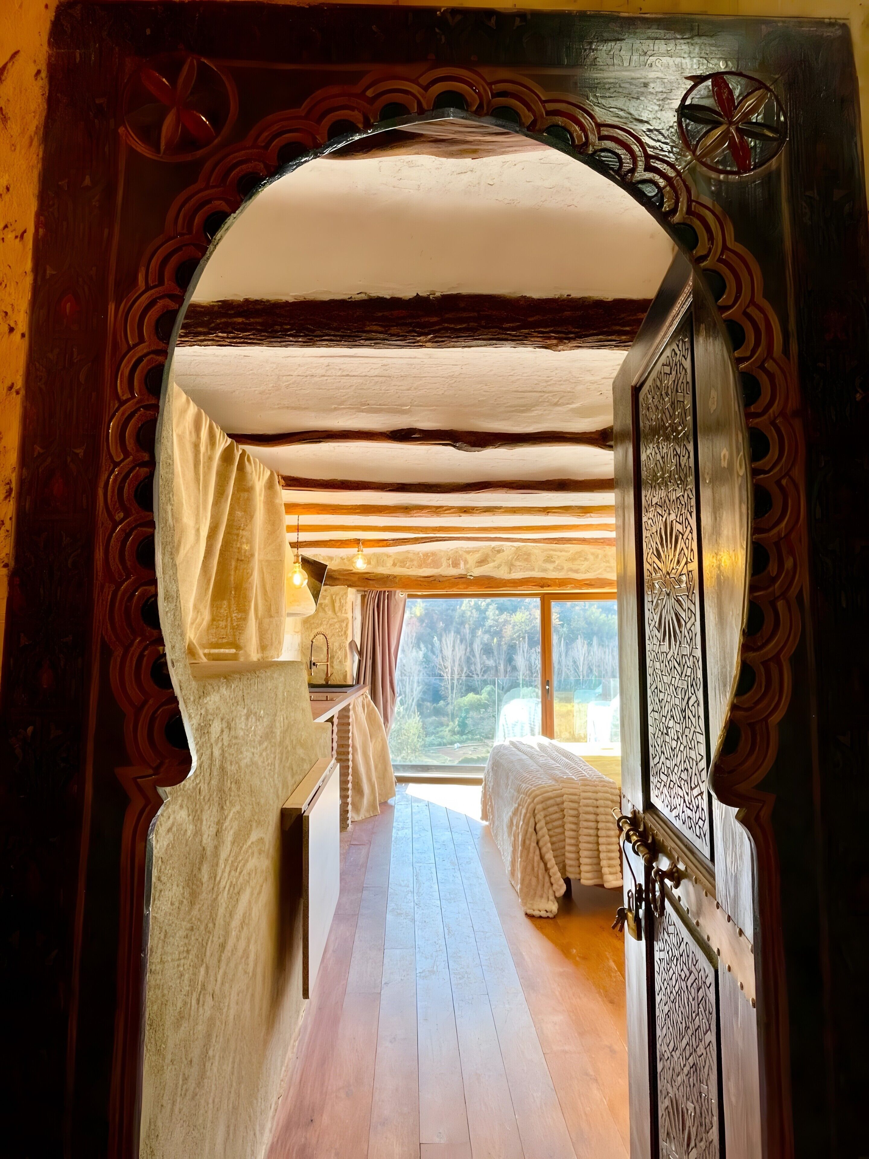 An arched doorway leading to a bedroom with a wooden floor, a bed, and a view of trees.