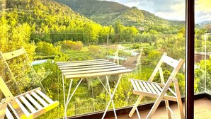 A balcony with a table and two chairs, overlooking a mountainous landscape with a river. - Apartment 'Duende' with Mountain View, Balcony and Air Conditioning (Olba)