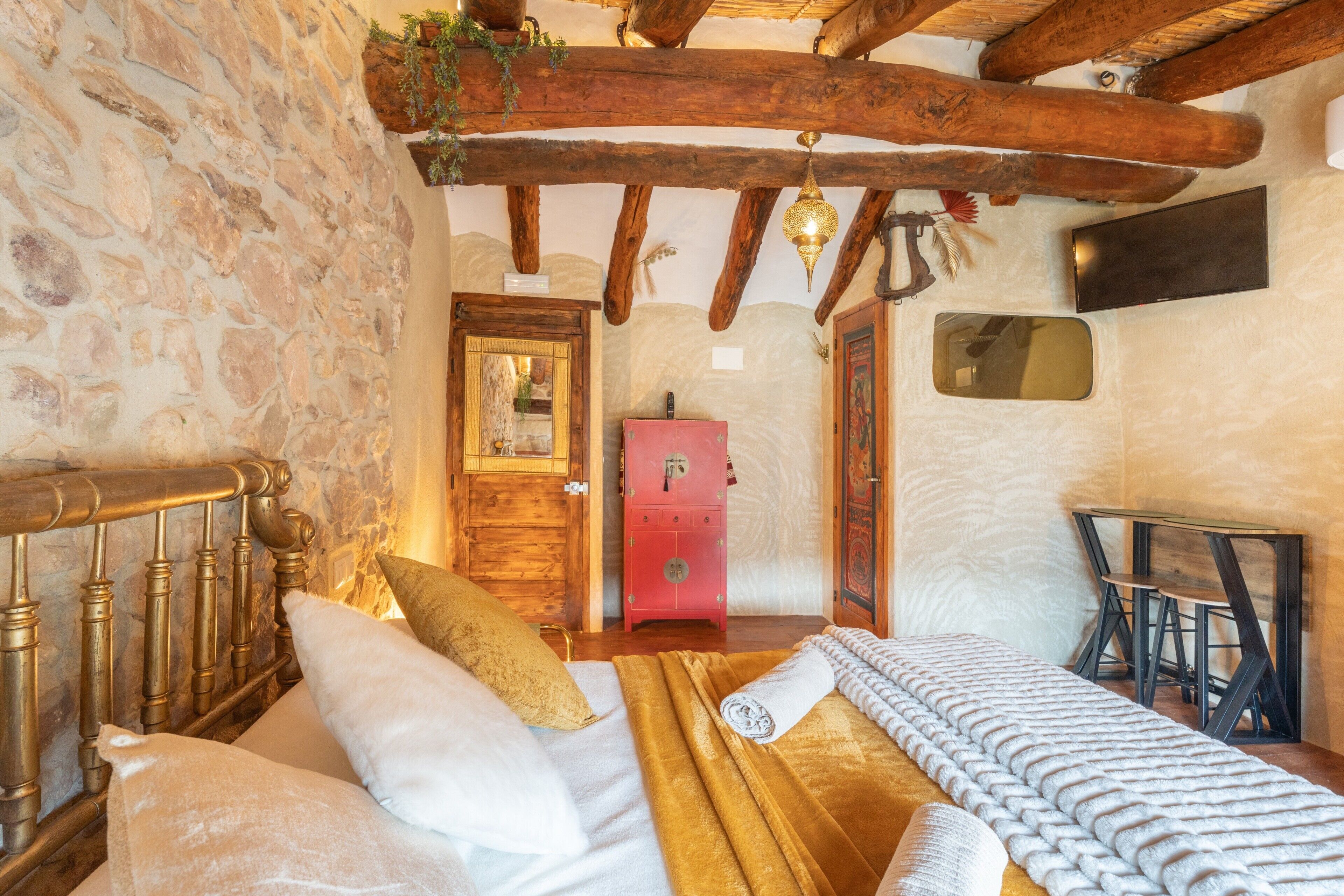 Ein rustikaler Raum mit Steinwänden, einem hölzernen Bett mit Kopfteil, einem roten Schrank und einem Holztisch mit Stühlen.