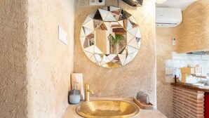 Ein Badezimmer mit rundem Spiegel, einem goldenen Waschbecken und einer Wand in roter Backsteinoptik.