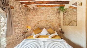 Dormitorio con paredes de piedra, una cama, almohadas y un espejo.