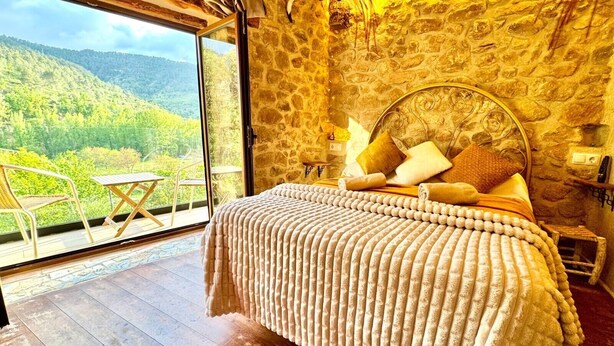 Ein Schlafzimmer mit Steinwand, Bett mit Kopfteil, Fenster und Balkon mit Tisch und Stühlen.