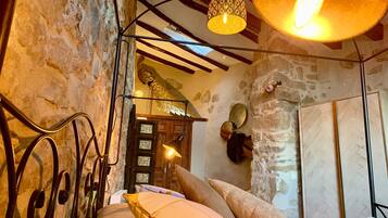 A rustic room with a stone wall, a wooden door, a bed with pillows, a hanging light fixture, and a mirror on the wall.