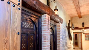 Una porta in legno con chiodi decorativi in metallo, un muro in mattoni e un lampadario.