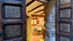Una porta in legno aperta, con elaborate decorazioni in metallo, dà accesso a una stanza con travi a vista e una parete in pietra.