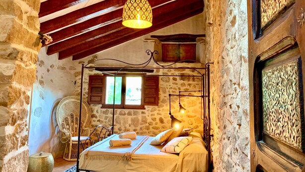 Una camera da letto rustica con un letto a baldacchino, pareti in pietra, soffitto in legno e una lampada a sospensione.
