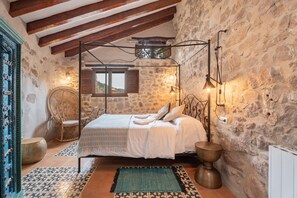 Ein rustikales Schlafzimmer mit Himmelbett, Steinwänden und Blick auf die Landschaft.