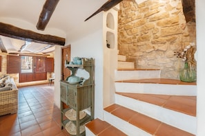 A rustic interior with a stone wall, wooden staircase, and a wicker sofa.