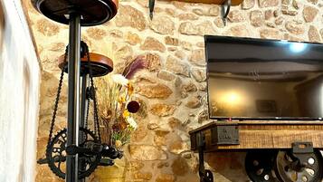 Un intérieur rustique avec un mur en pierre, une étagère en bois sur laquelle est posée une horloge, un tabouret de bar ancien et un chariot à roulettes.