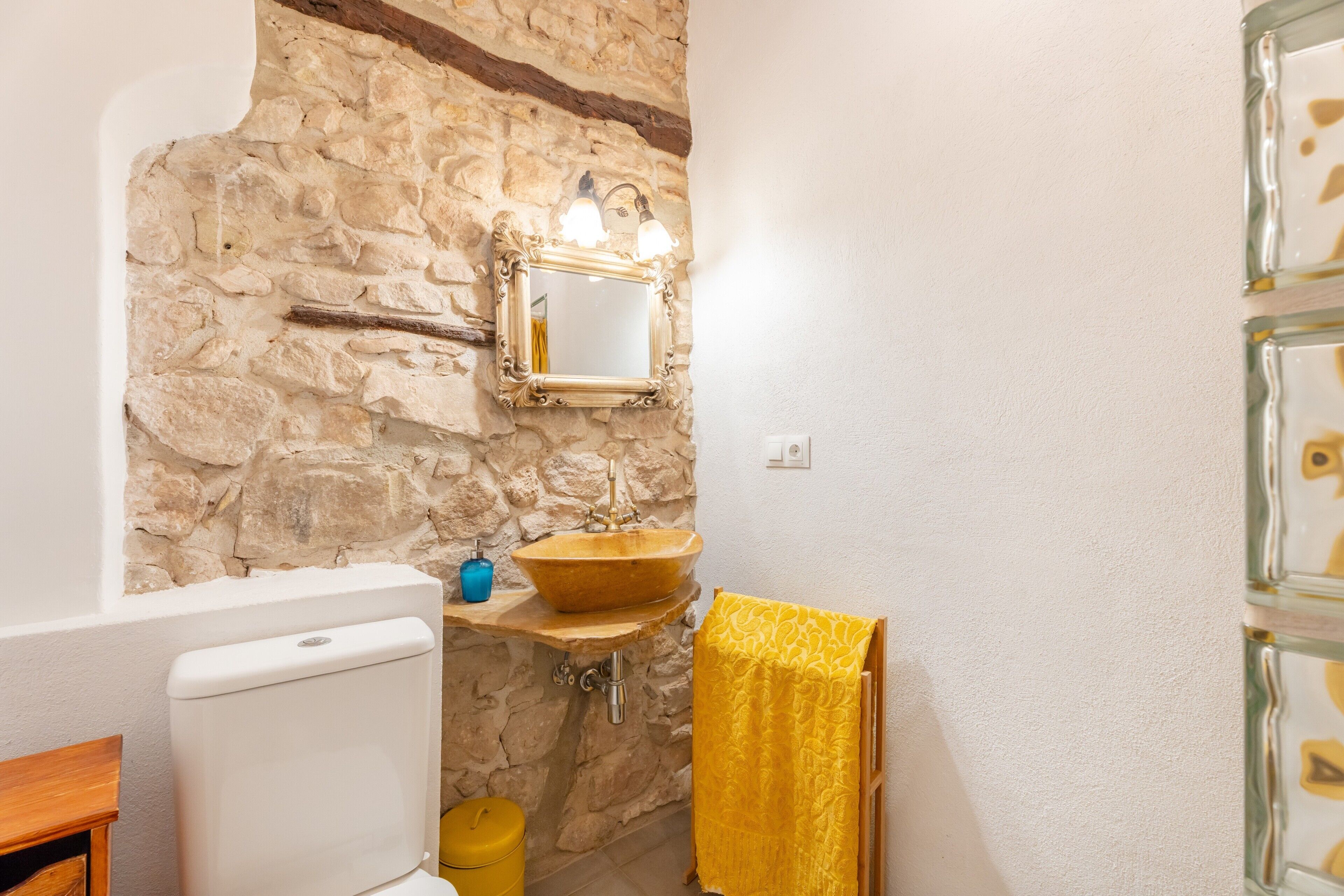 A bathroom with a stone wall, a wooden sink, a mirror, and a yellow towel.
