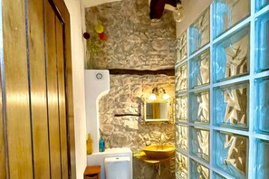 Ein Badezimmer mit Steinwand, Holztür, Waschbecken und Spiegel.