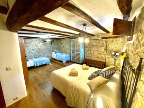Ein rustikales Schlafzimmer mit sichtbaren Holzbalken, einer Steinwand und einem Bett mit weißer Bettdecke.